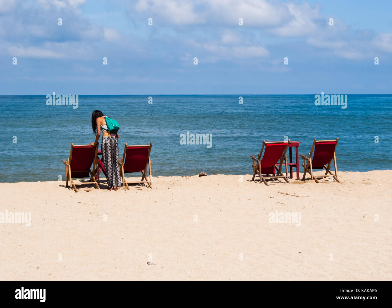 Chaises de plage mis en place par paires avec un parapluie repliées dans entre eux sur le bord de la plage avec l'eau et le ciel bleu en arrière-plan. Banque D'Images