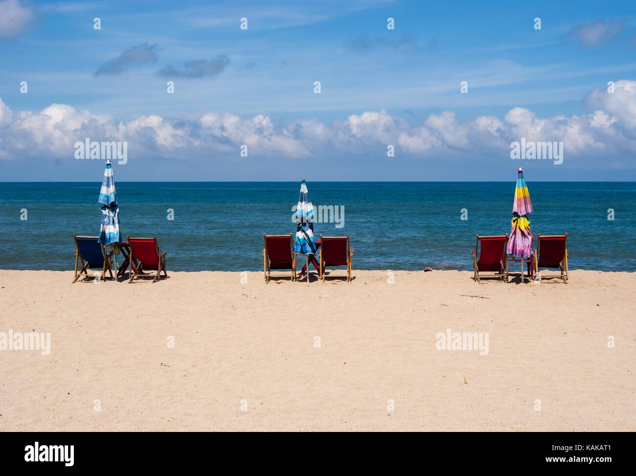 Chaises de plage mis en place par paires avec un parapluie repliées dans entre eux sur le bord de la plage avec l'eau et le ciel bleu en arrière-plan. Banque D'Images
