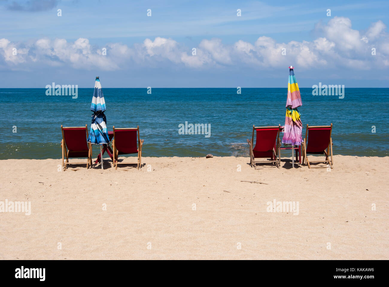 Chaises de plage mis en place par paires avec un parapluie repliées dans entre eux sur le bord de la plage avec l'eau et le ciel bleu en arrière-plan. Banque D'Images
