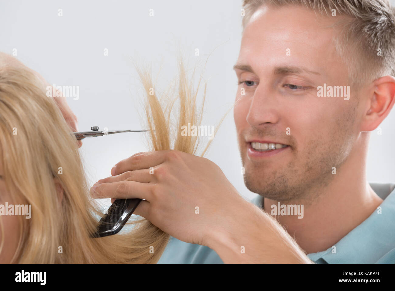 Happy young male hairdresser cutting customer's hair at salon Banque D'Images