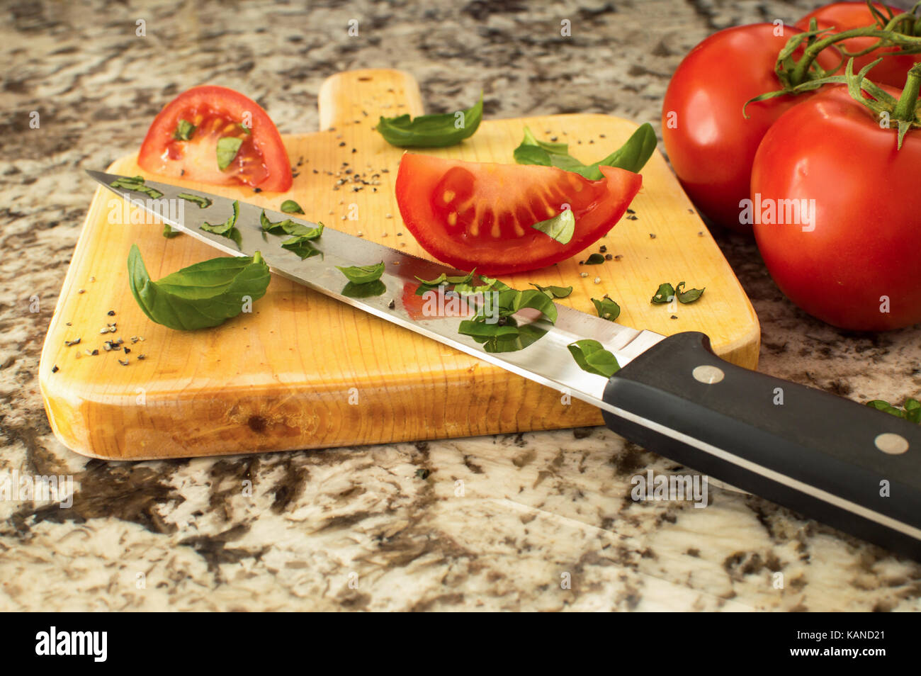 Une de tranches de tomate au basilic sur une planche à découper, un couteau et un tas de tomates sur la vigne. Banque D'Images