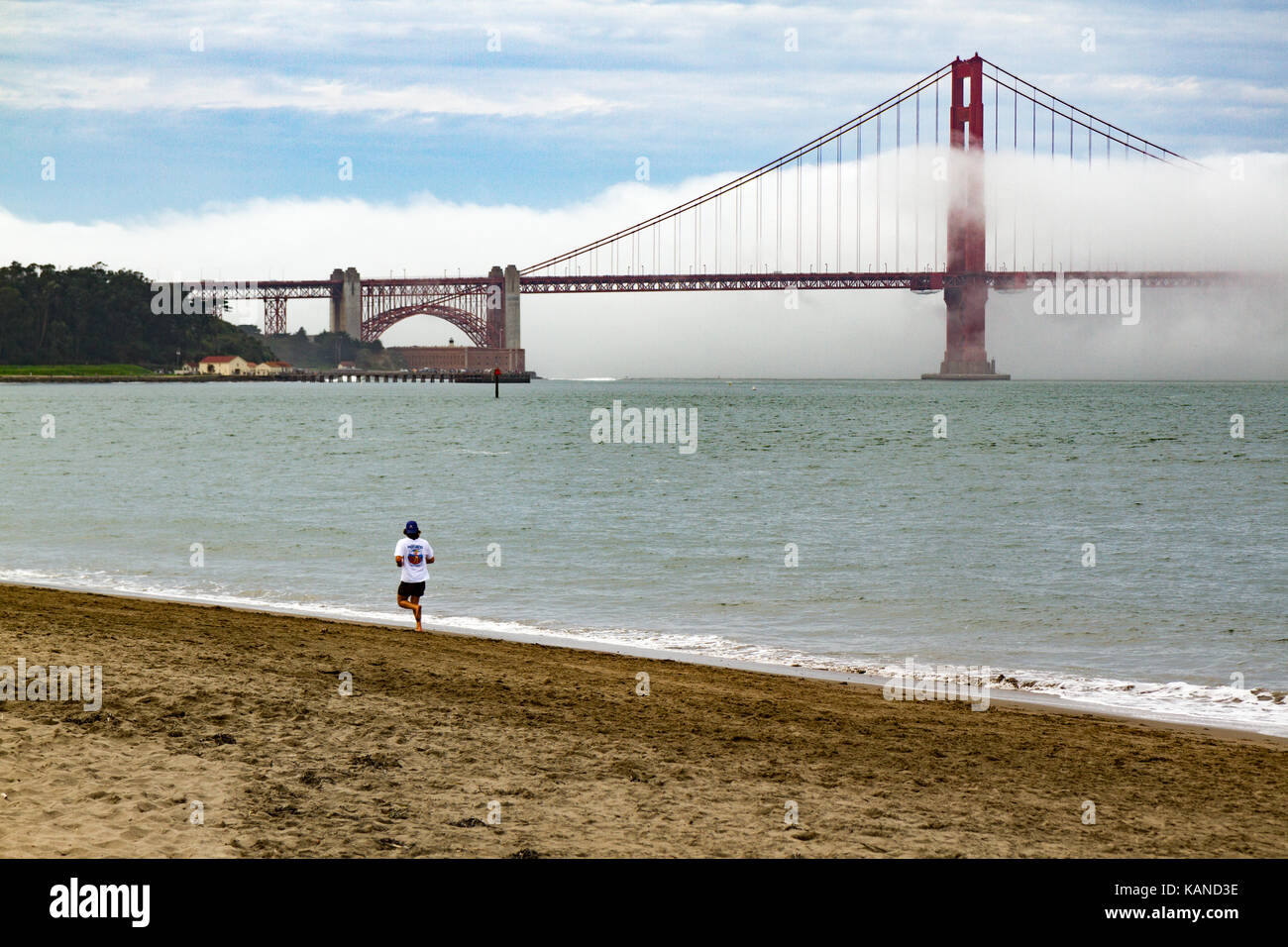 Personne le jogging sur plage en face du Golden Gate Bridge, San Francisco, Californie, USA. Pont est en partie dans le brouillard, Banque D'Images