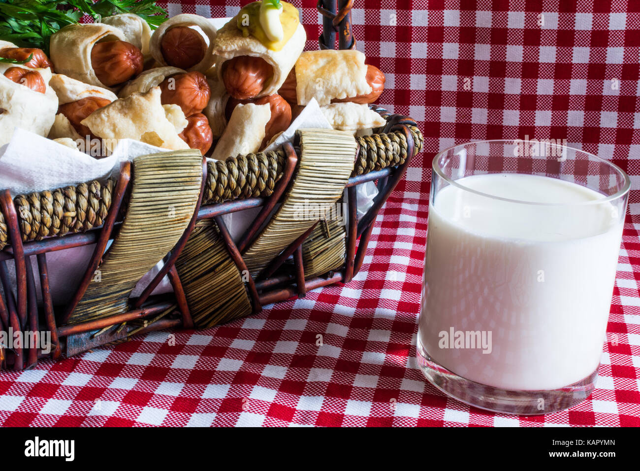 Panier en osier avec artisan mini hot dog (la saucisse dans la pâte) et un verre de lait de vache du village, sur un fond à carreaux Banque D'Images