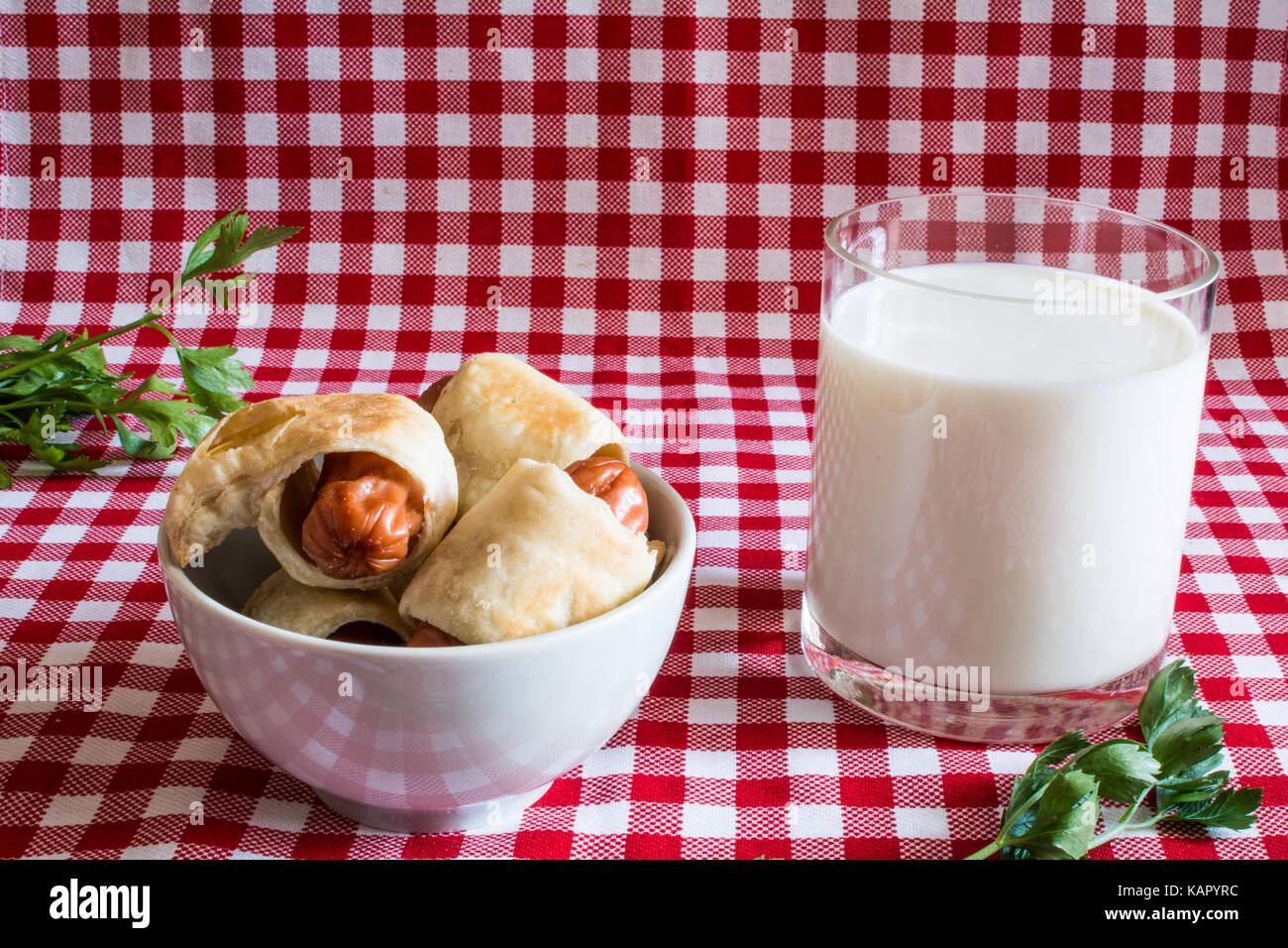 Plaque avec mini hot dog (maison de la saucisse dans la pâte) et un verre de lait de vache avec du persil sur un fond à carreaux. le 18 juillet, l'Amérique de célébrité Banque D'Images