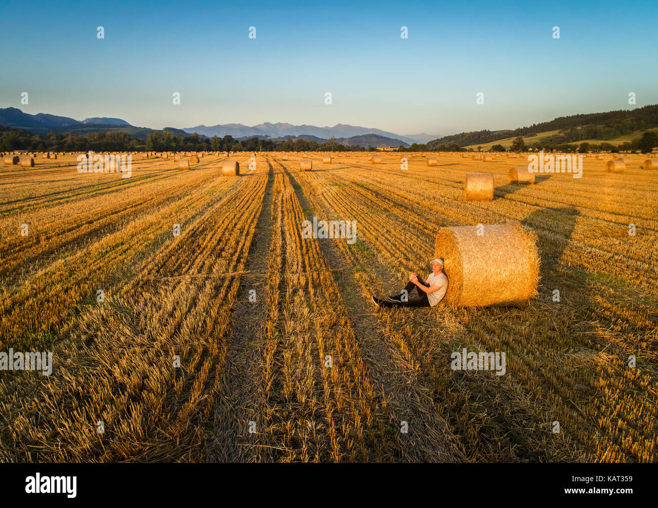 Jeune homme jouit de coucher du soleil à un champ avec des bottes de foin Banque D'Images
