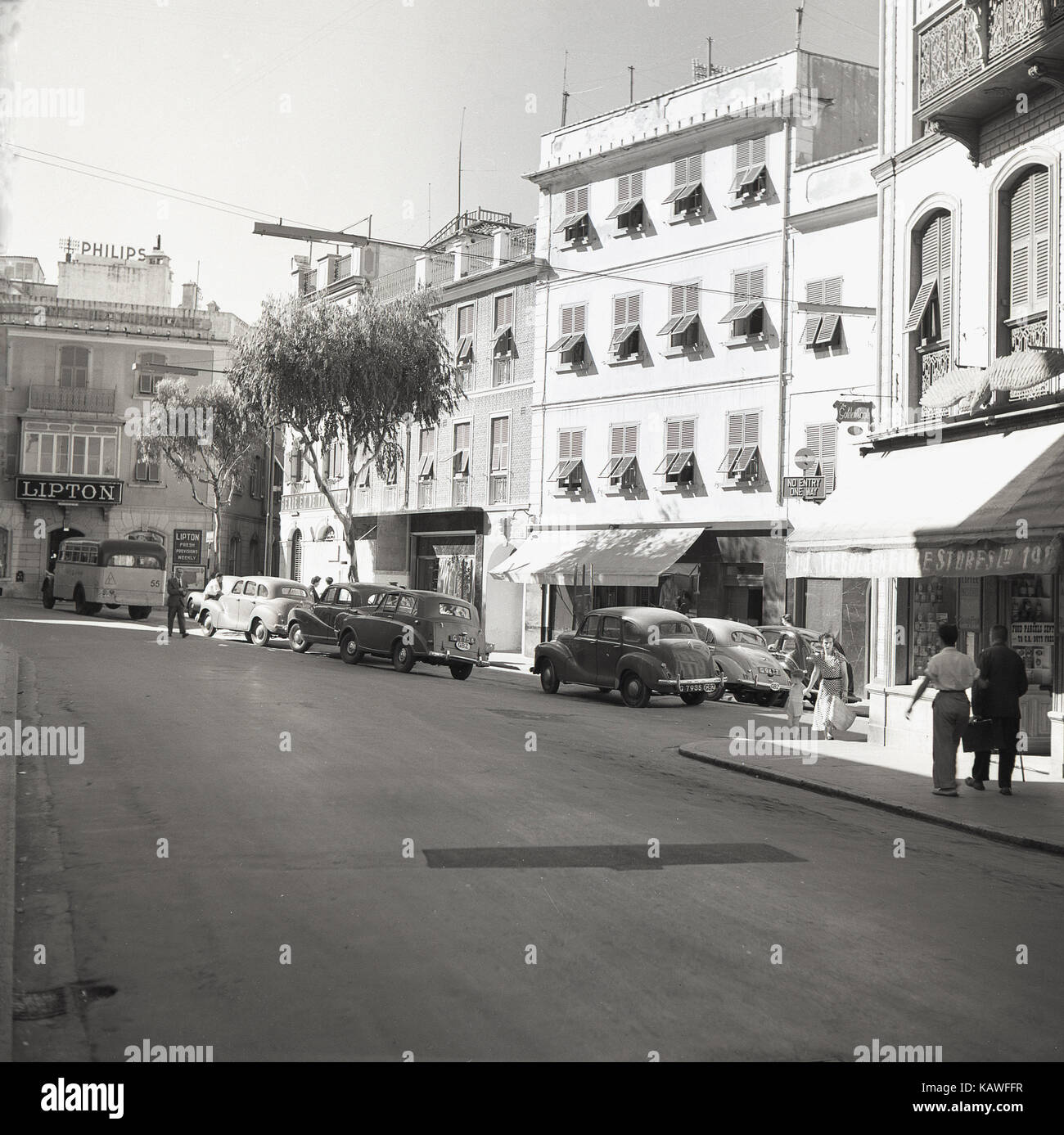 Années 1950, tableau historique par J Allan Paiement de Passage du Giro, Southport, Gibraltar, montrant des voitures, des boutiques et un appelé publicité Lipton provisions fraîches chaque semaine. Banque D'Images