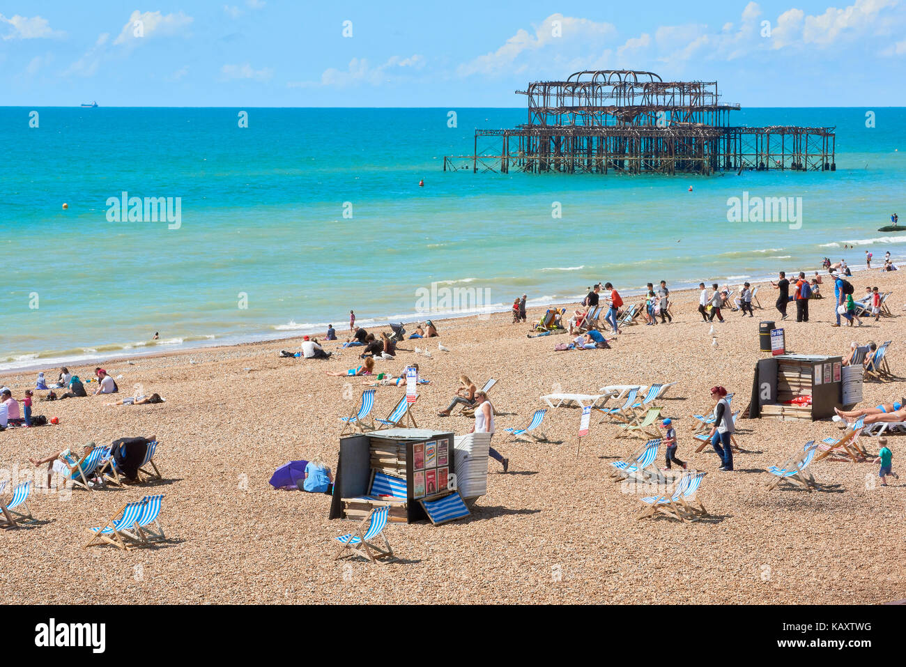 Amateurs de profiter du soleil à Brighton, endommagée par l'incendie avec Brighton West Pier squelette dans l'arrière-plan. Banque D'Images