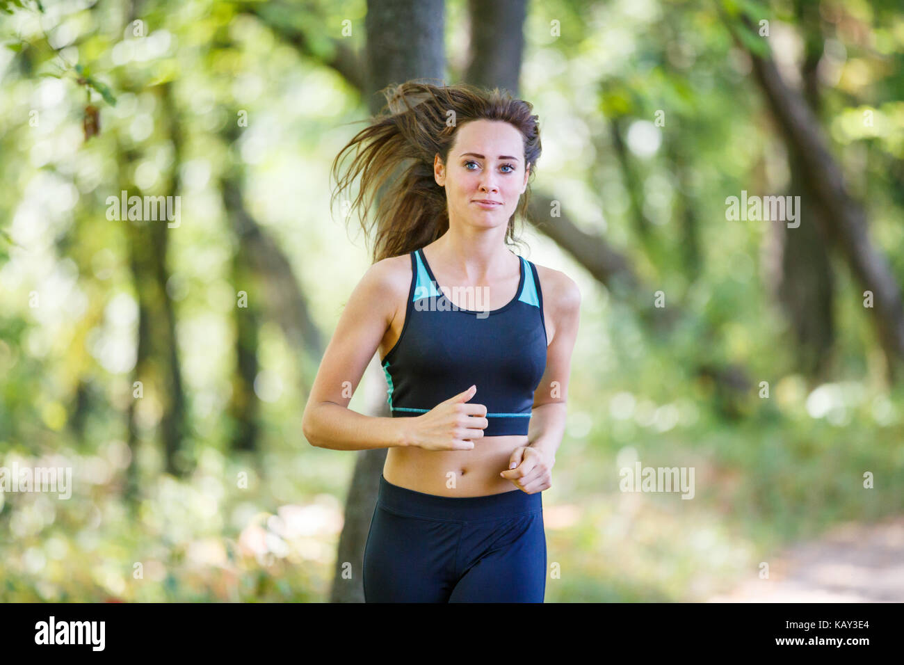 Young smiling sporty woman running in park le matin. fitness petite fille jogging en parc. trail running concept background Banque D'Images