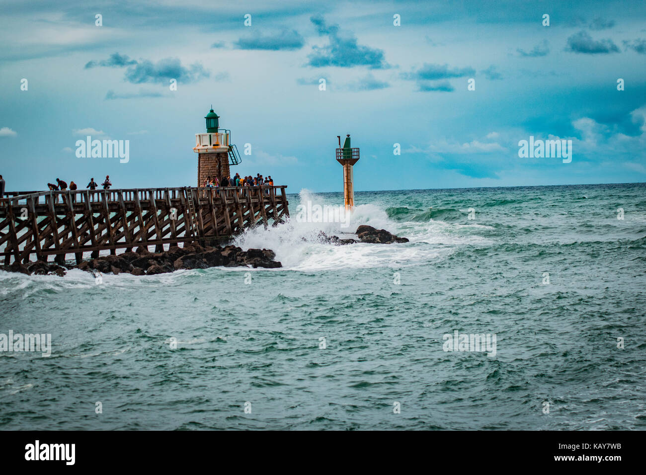 C'est une qualité d'image d'une scène de la mer avec une jetée, phare, le fracas des vagues, des rochers et un ciel bleu avec des nuages qui complètent l'image. Banque D'Images