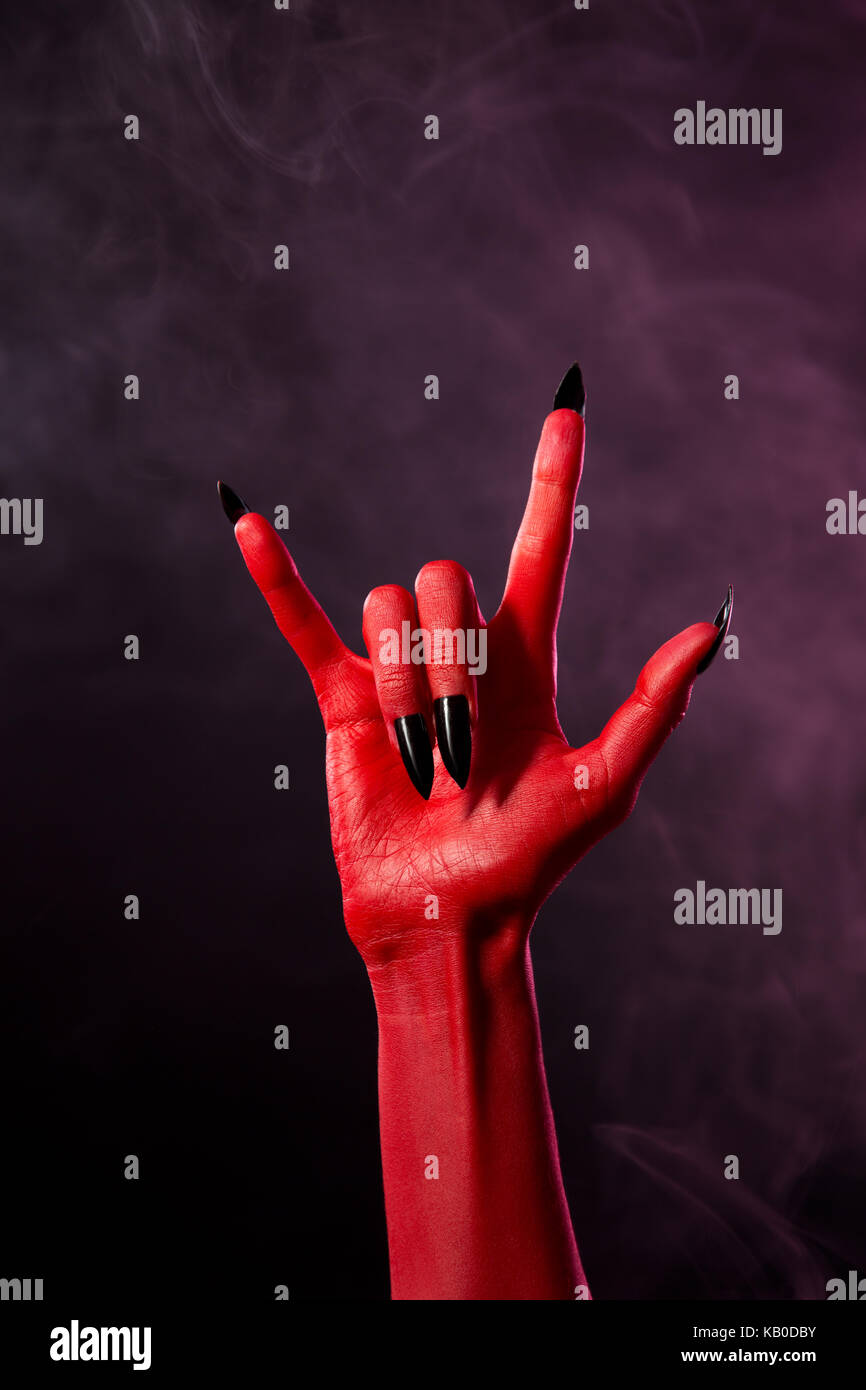 La main du diable rouge avec noir ongles pointus, studio shot sur fond fumé Banque D'Images