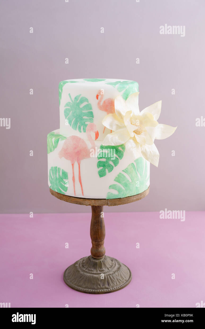 Gâteau de mariage tropical à deux niveaux avec du fondant, le pain azyme tropicales feuilles et flamants roses avec une grosse fleur sur déclaration d'or cake stand en bois Banque D'Images