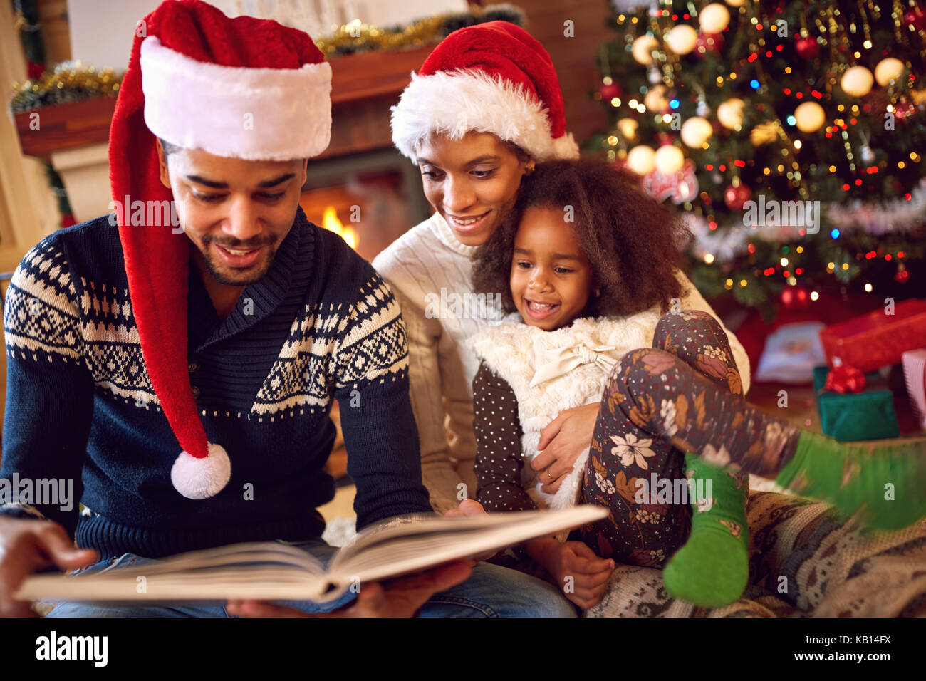 Happy afro american family lire un livre à la cheminée la veille de Noël. famille avec enfant qui célèbre Noël Banque D'Images