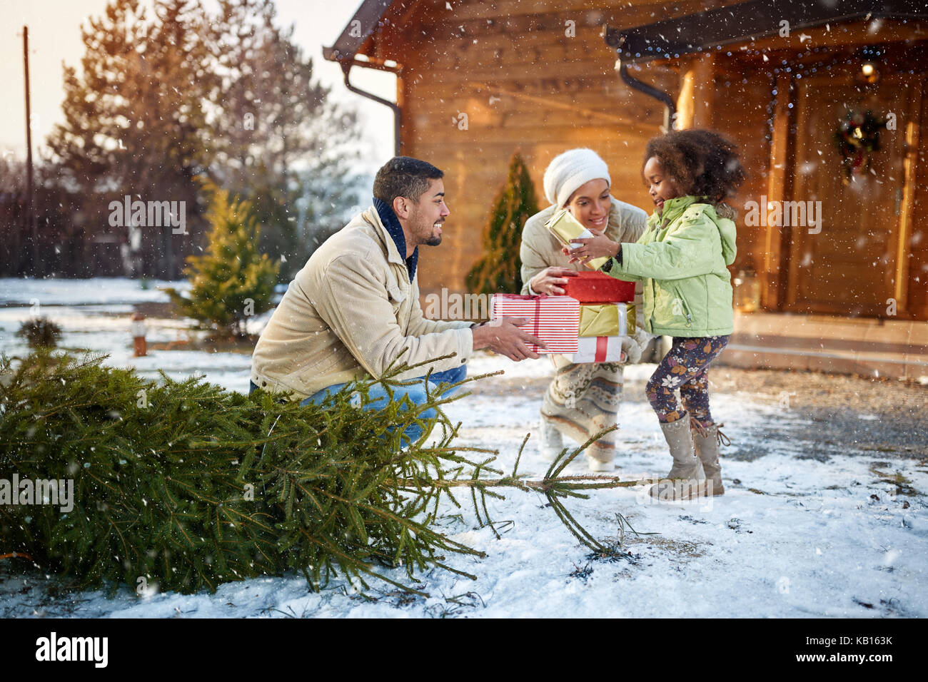 Peu d'afro-américaine fille avec des cadeaux de Noël avec les parents, d'une face de la maison en bois Banque D'Images