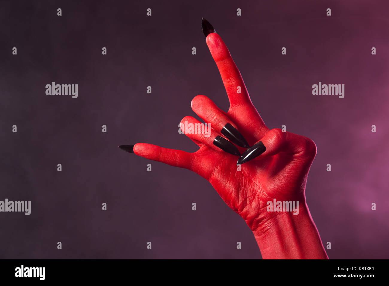 La main du diable rouge noir avec clous, heavy metal geste, studio shot sur fond fumé Banque D'Images