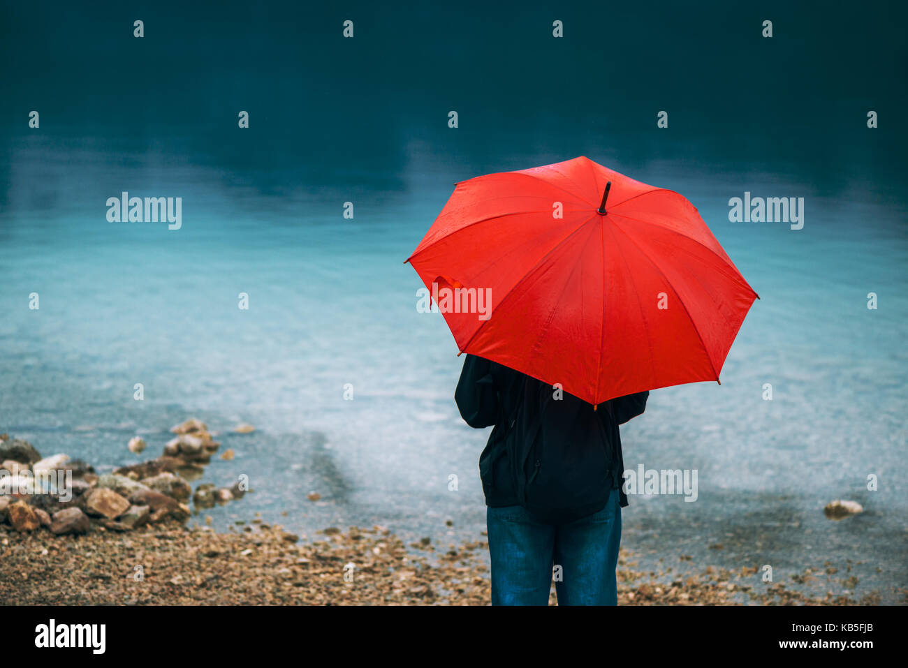 Femme avec parapluie rouge prévoit de la pluie en face d'un lac. triste et solitaire à la personne de sexe féminin dans la distance. Banque D'Images