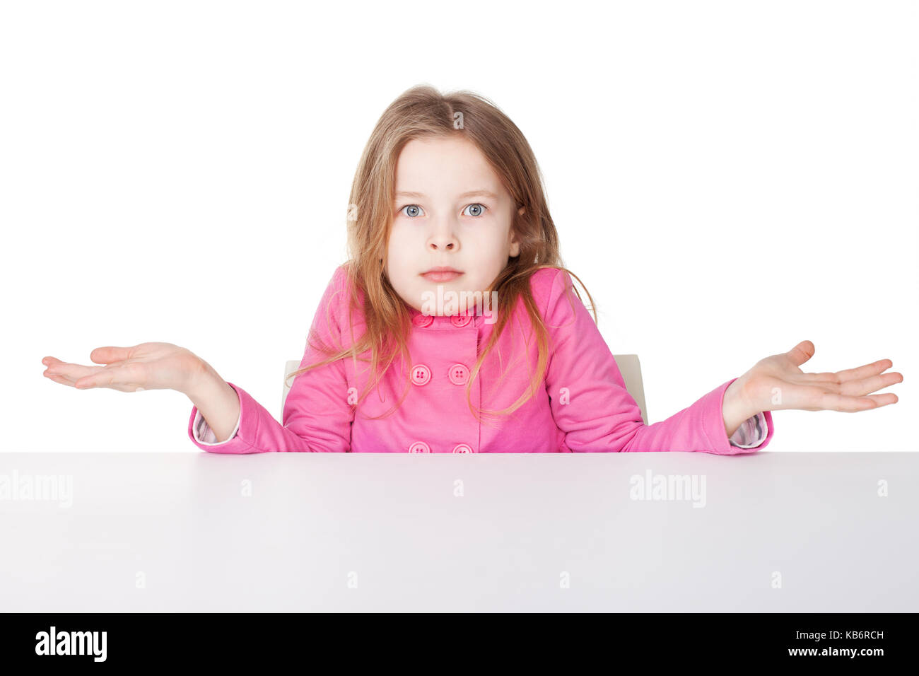 Cute little girl in red shirt haussant les épaules tout en étant assis à table isolé sur fond blanc Banque D'Images