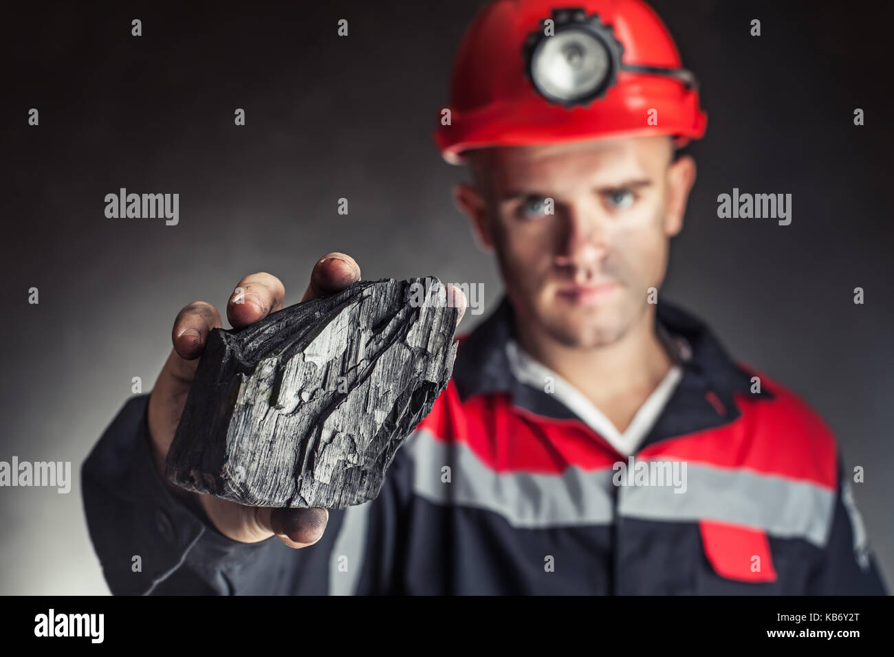 Mineur de charbon montrant bloc de charbon contre un fond sombre Banque D'Images