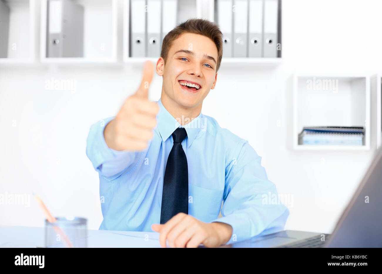 Portrait of young laughing woman showing Thumbs up sur son lieu de travail à bright office Banque D'Images