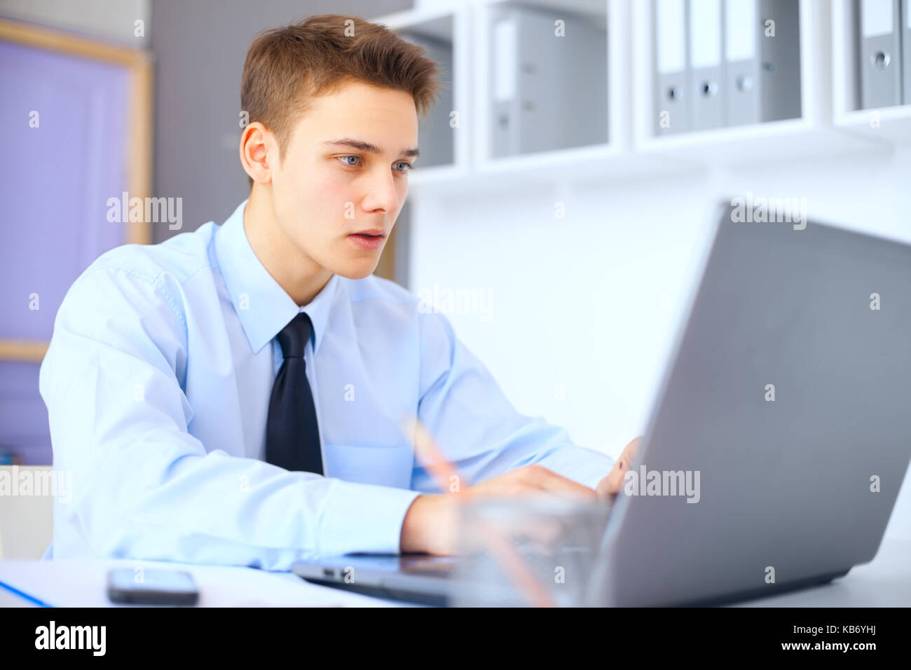 Les jeunes serious businessman working on laptop in bright office Banque D'Images
