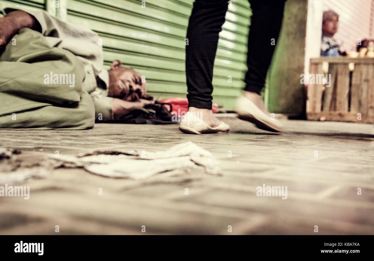 Indonesian man sans domicile fixe de dormir sur le trottoir recroquevillé dans une balle alors que les gens à pied nonchalamment par sans donner une seconde pensée en Asie Banque D'Images