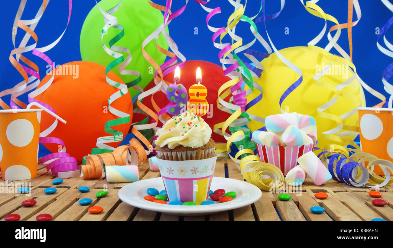 98 birthday cupcake avec bougies sur table en bois rustique avec fond de ballons colorés verres en plastique bonbons sur mur bleu en arrière-plan Banque D'Images