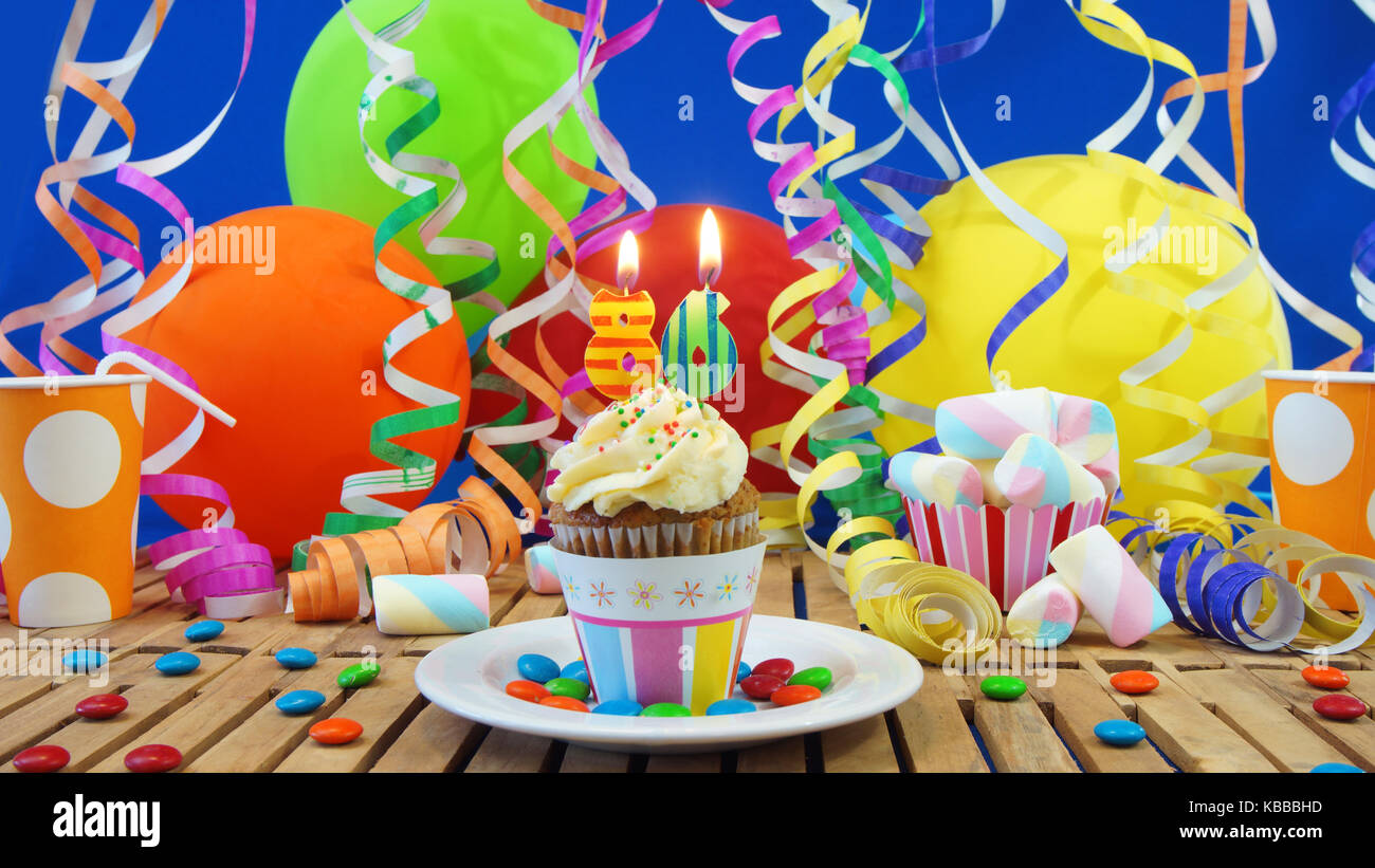 86 birthday cupcake avec bougies sur table en bois rustique avec fond de ballons colorés verres en plastique bonbons sur mur bleu en arrière-plan Banque D'Images