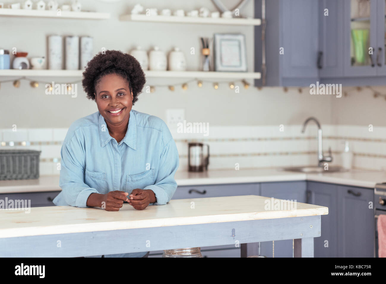 Souriante jeune femme africaine appuyée sur son île de cuisine Banque D'Images