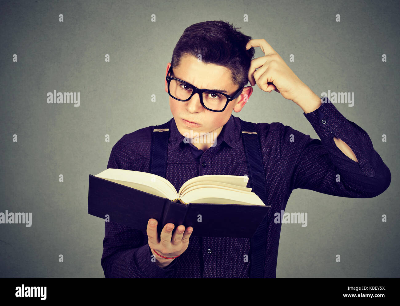 Jeune homme confus dans les verres perplexe après la lecture d'un livre Banque D'Images