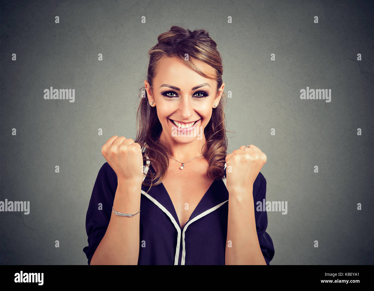 Heureux gagnant. femme exulte poings pompage célèbre son succès sur fond de mur gris Banque D'Images