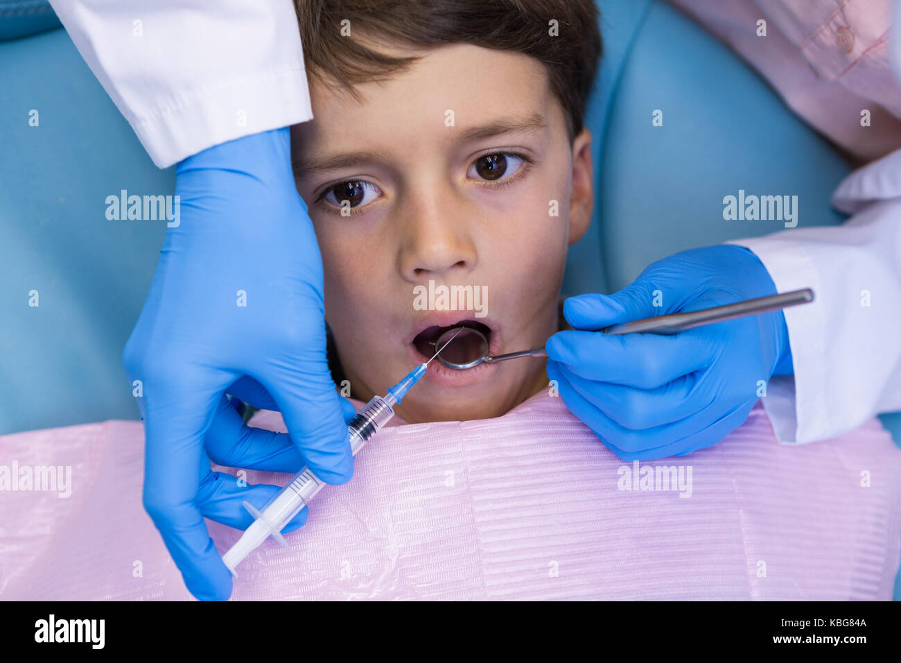 Portrait de dentiste holding syringe, tout en traitant les garçon à la clinique médicale Banque D'Images