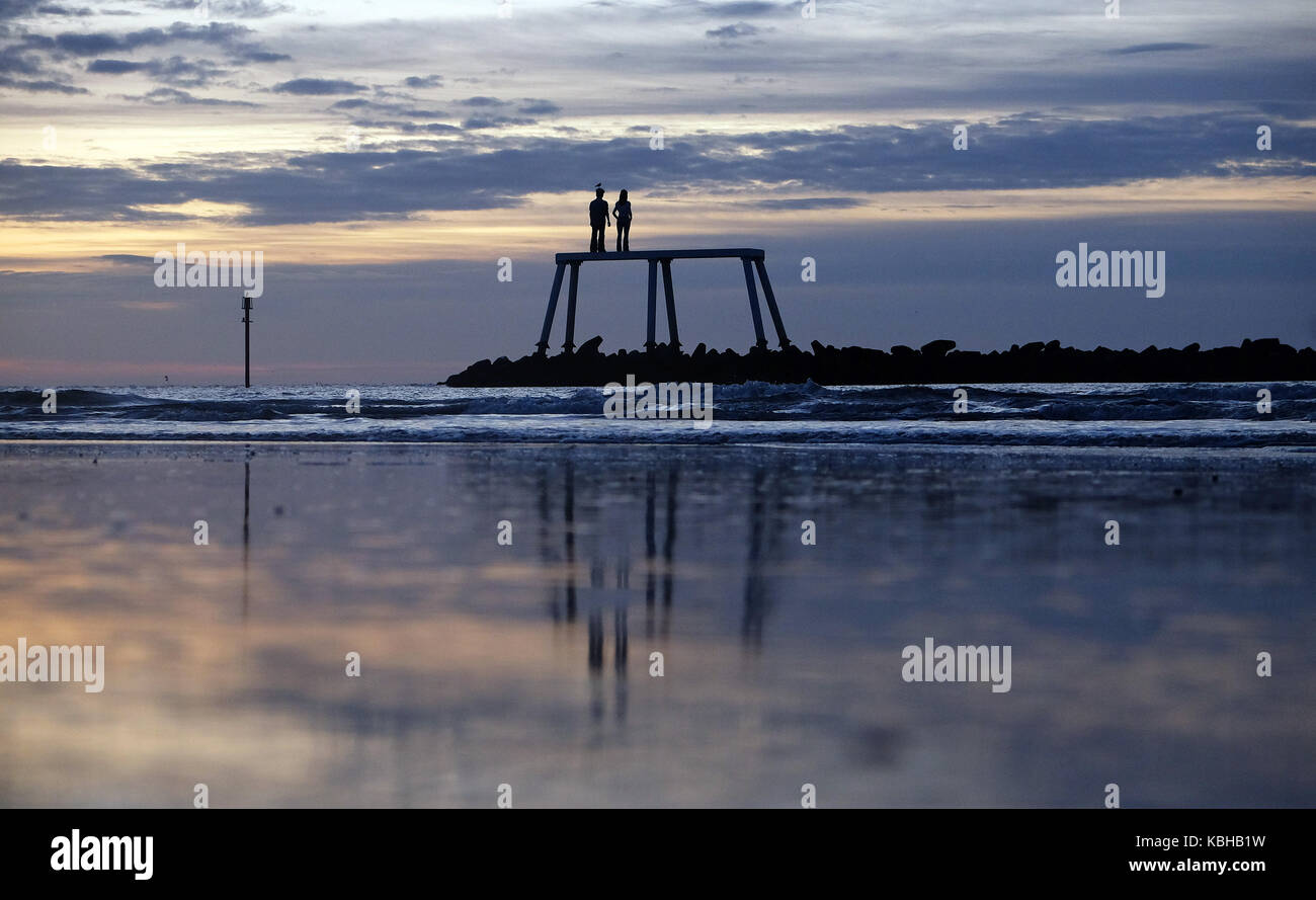 Le soleil d'automne s'élève au-dessus de la mer du Nord devant le couple par l'artiste Sean Henry à Newbiggin-by-the-Sea, Northumberland, alors que la Grande-Bretagne est sur le point de connaître de fortes pluies et des gales tandis que les restes de l'ouragan Lee ajoutent un oomph supplémentaire à un système de basse pression qui traverse l'Atlantique, ont déclaré des prévisionnistes. Banque D'Images