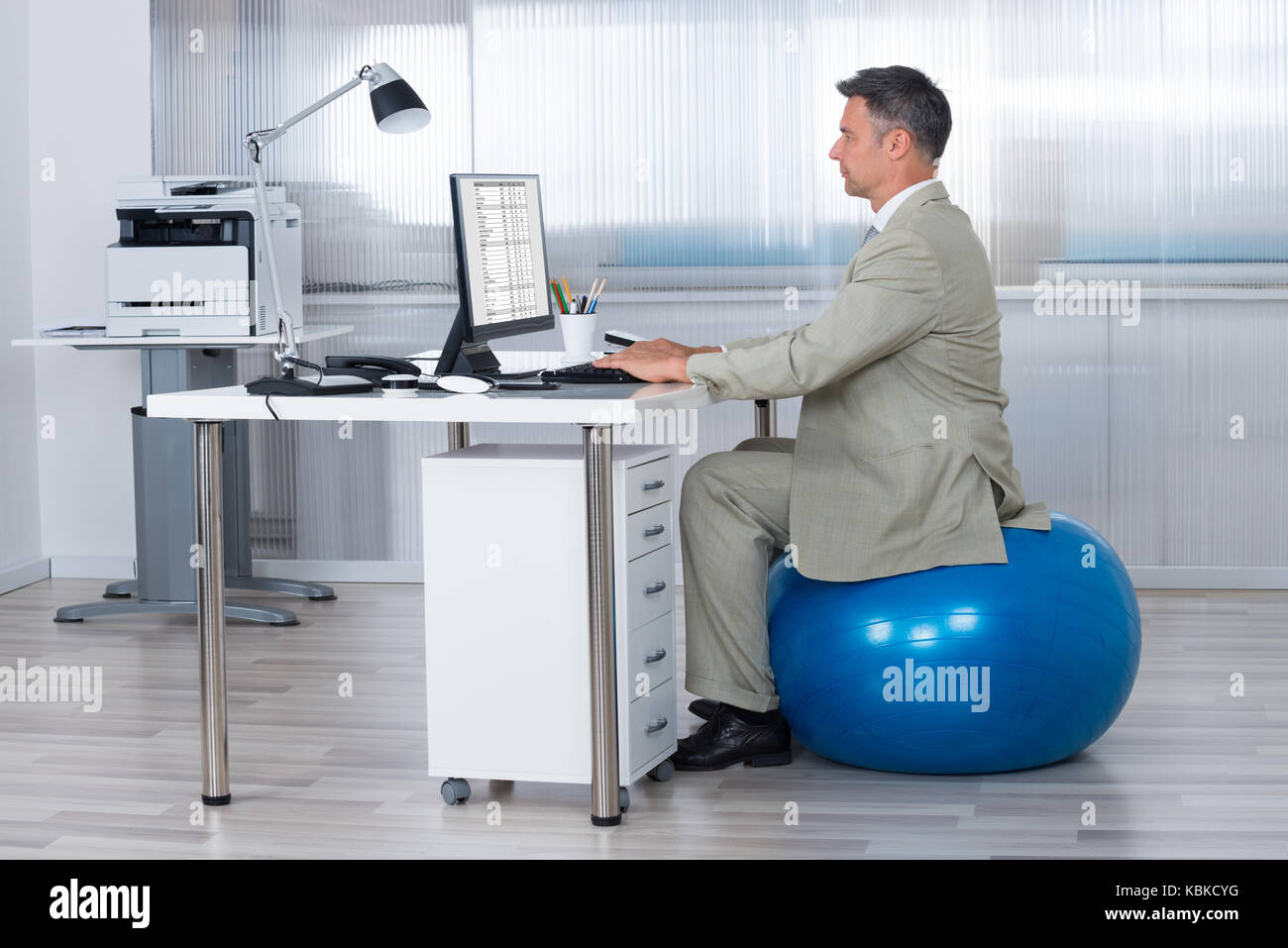 Vue latérale du businessman using computer while sitting on exercise ball at office Banque D'Images