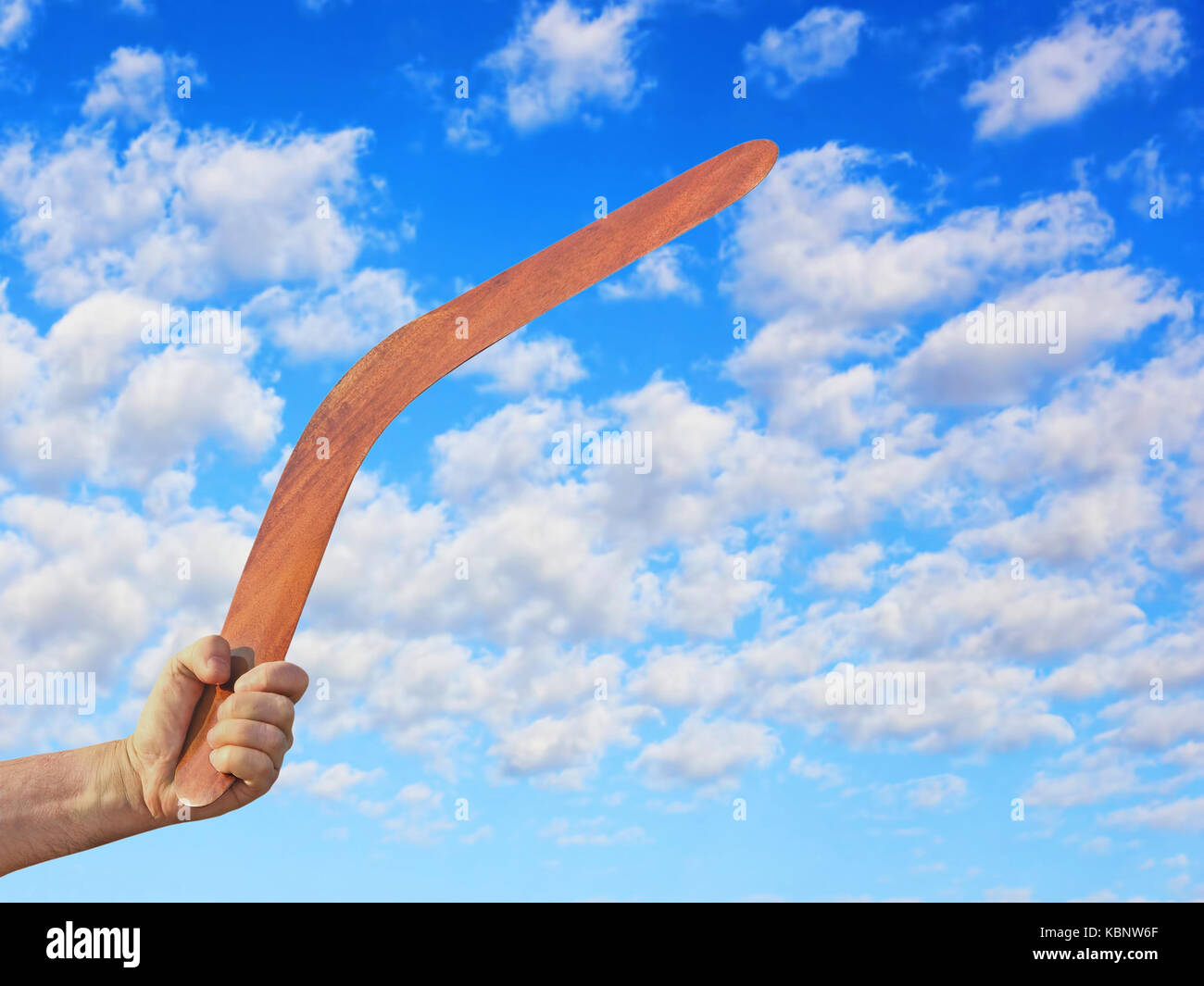 Boomerang australien dans la main des hommes pris libre contre de nuageux ciel bleu. Banque D'Images