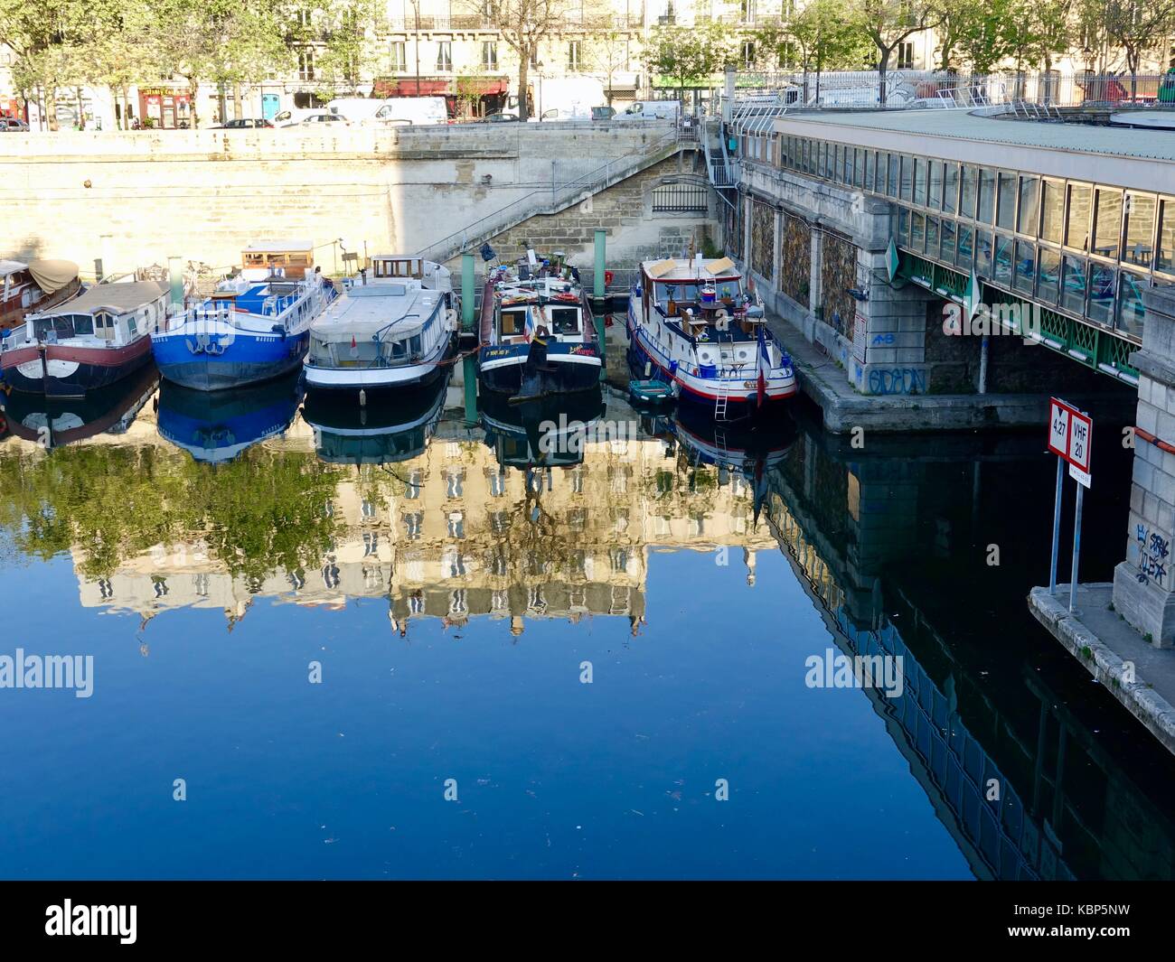 La réflexion des immeubles d'appartements dans l'eau au Bassin de l'Arsenal avec de l'eau d'un bleu profond et ses bateaux amarrés à côté de la station de métro, Paris, Fr. Banque D'Images
