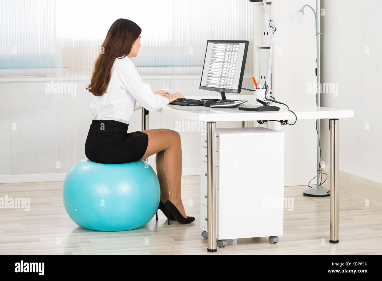 Vue latérale du young businesswoman using computer, assis sur pilates ball in office Banque D'Images