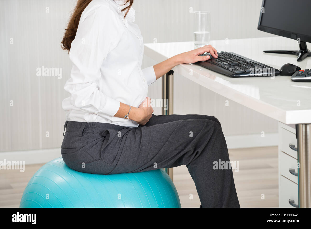 Side view midsection of pregnant businesswoman using computer while sitting on exercise ball in office Banque D'Images
