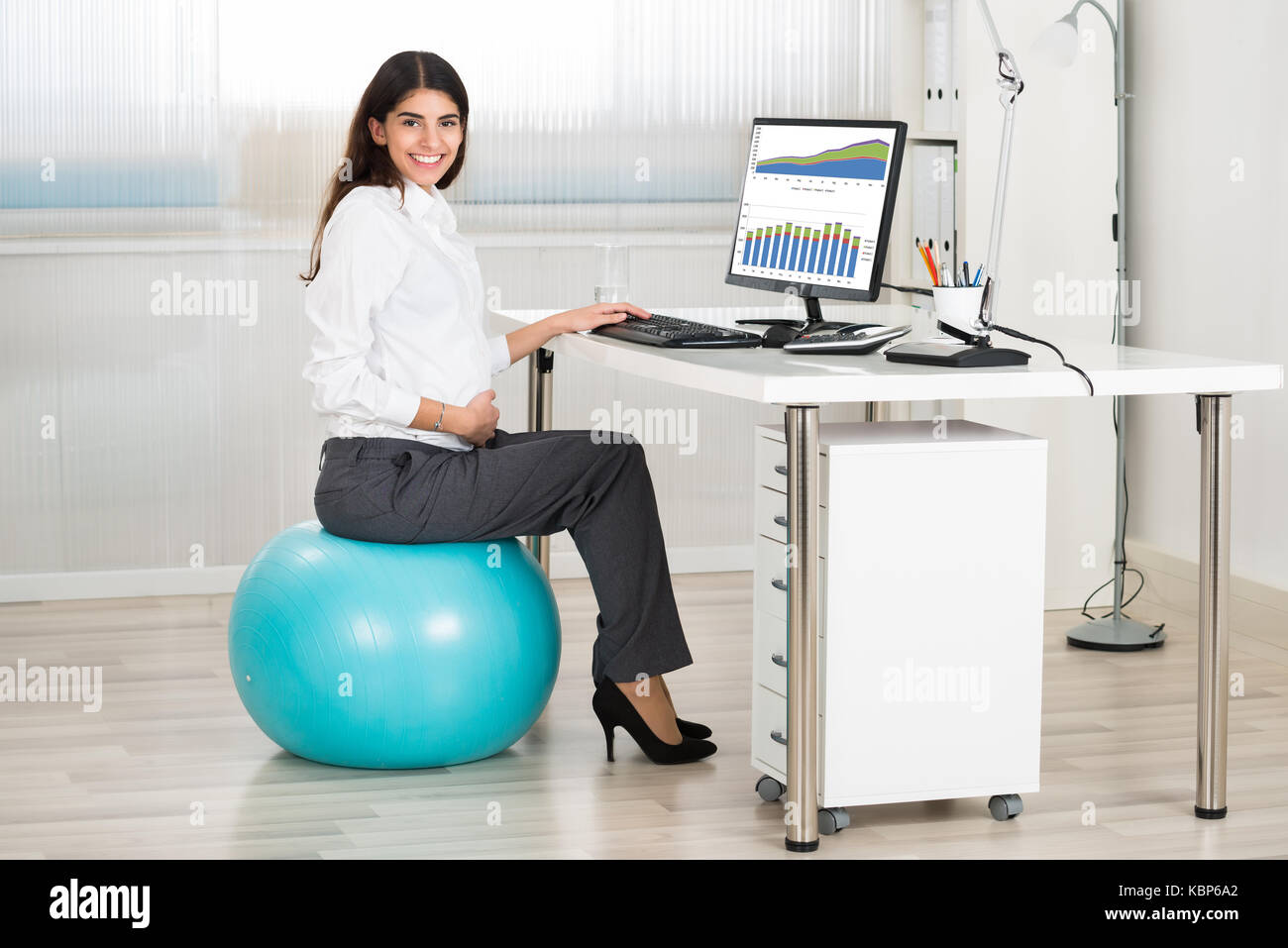Vue du côté des femmes enceintes businesswoman using computer while sitting on exercise ball in office Banque D'Images