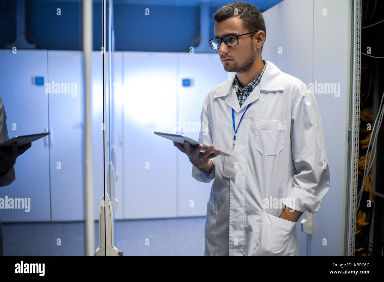 Portrait de jeune ingénieur réseau holding digital tablet debout entre les cabinets de serveurs dans le centre de recherches supercalculateur Banque D'Images