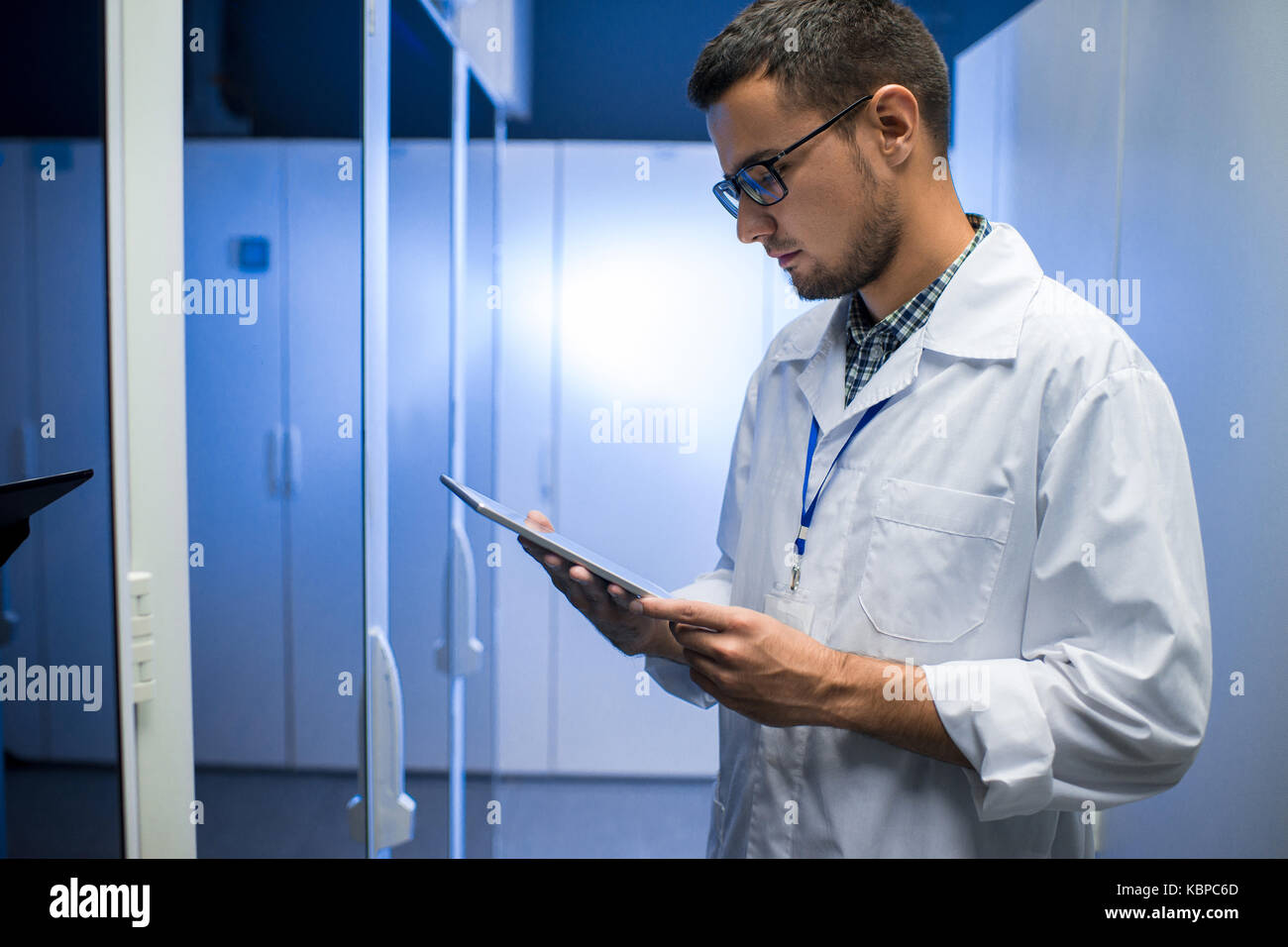 Vue de côté portrait de jeune ingénieur réseau looking at digital tablet debout entre les cabinets de serveurs dans le centre de recherches supercalculateur Banque D'Images