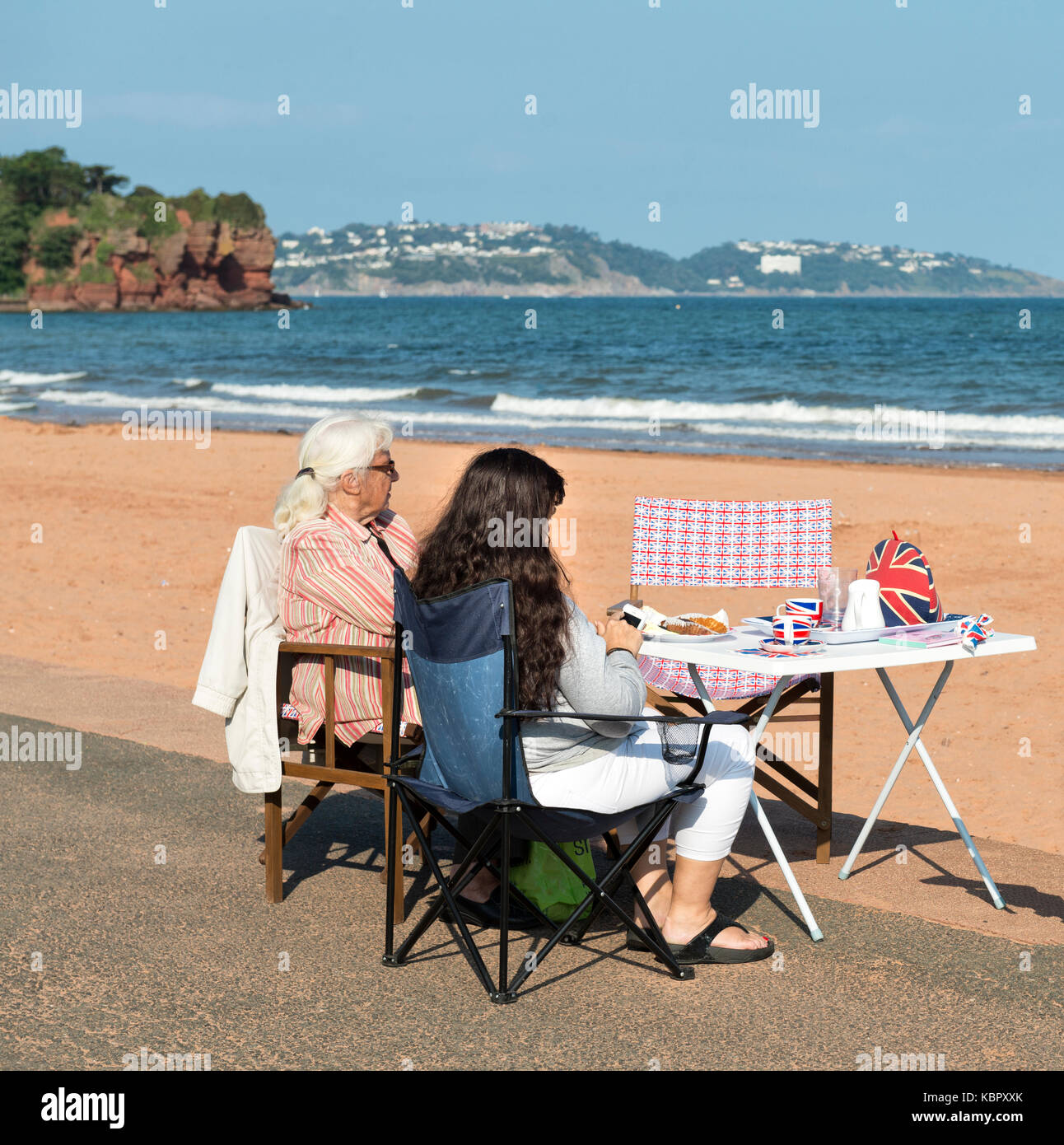 Une mère et sa fille se détendre à la plage de sable à l'extérieur de leur cabane de plage de goodrington sands paignton, bénéficiant d'une marque très britannique tasse de thé. Banque D'Images