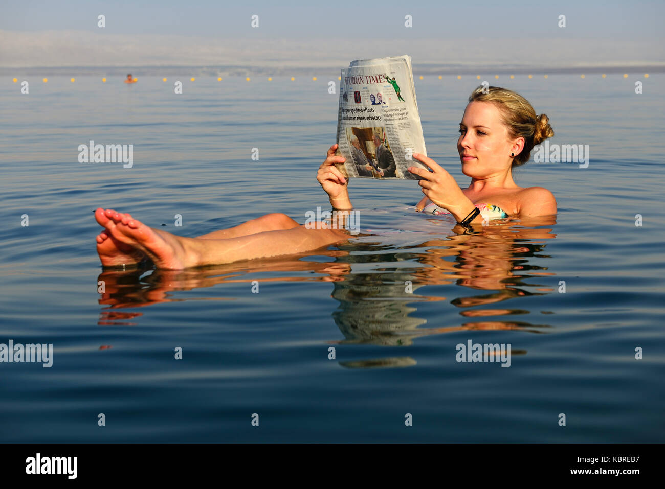 Jeune femme lit flottant journal en Mer Morte, Jordanie Banque D'Images