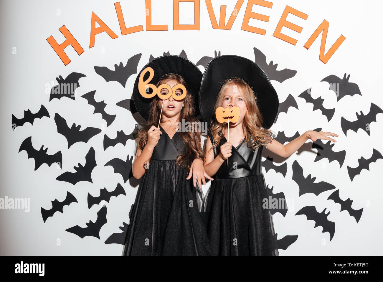 Couple de deux drôles de jolies petites filles vêtues de costumes d'halloween masques holding et posant avec les chauves-souris sur un arrière-plan Banque D'Images