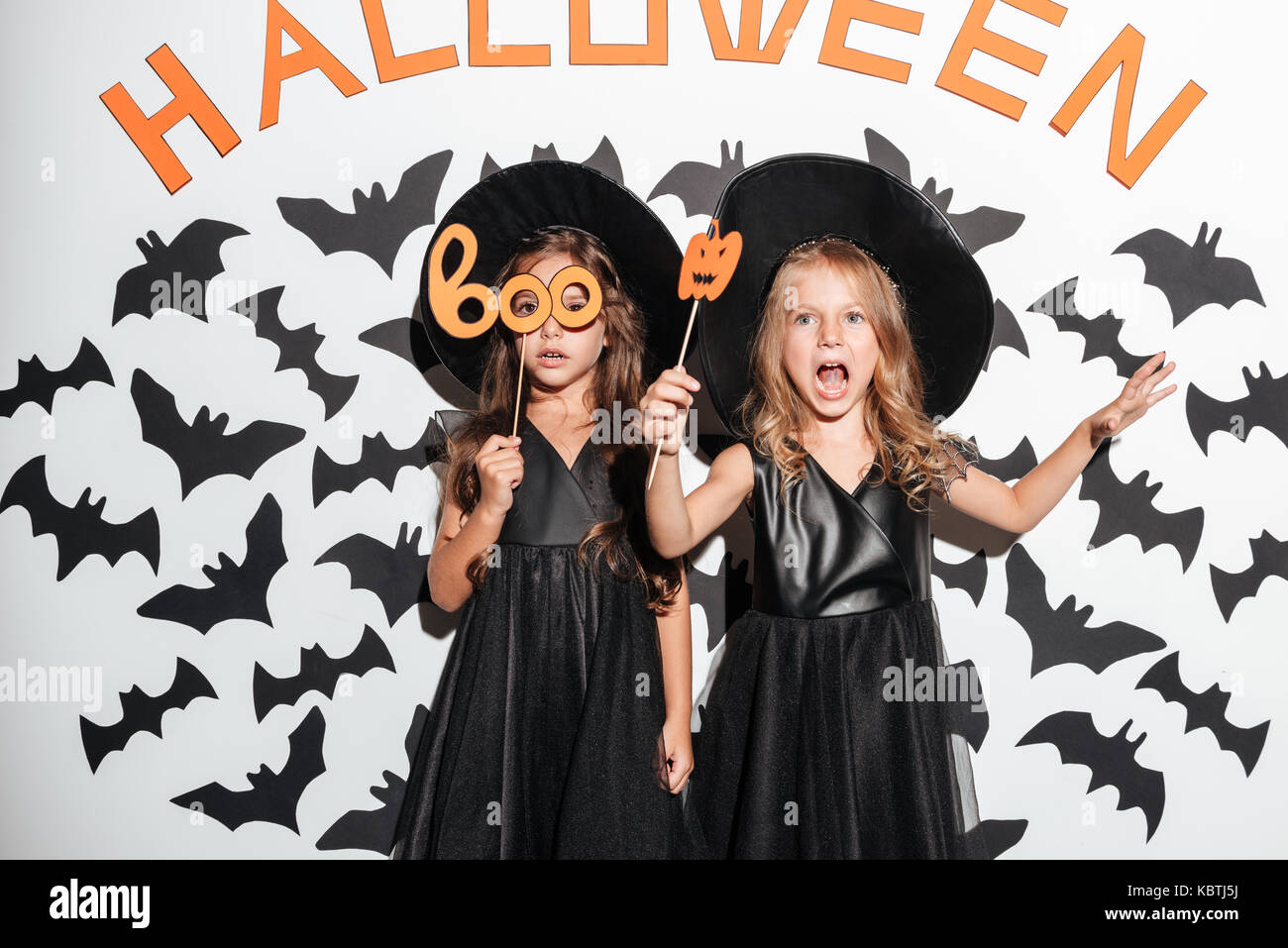 Couple de deux professionnels drôles de petites filles vêtues de costumes d'halloween masques holding et posant avec les chauves-souris sur un arrière-plan Banque D'Images