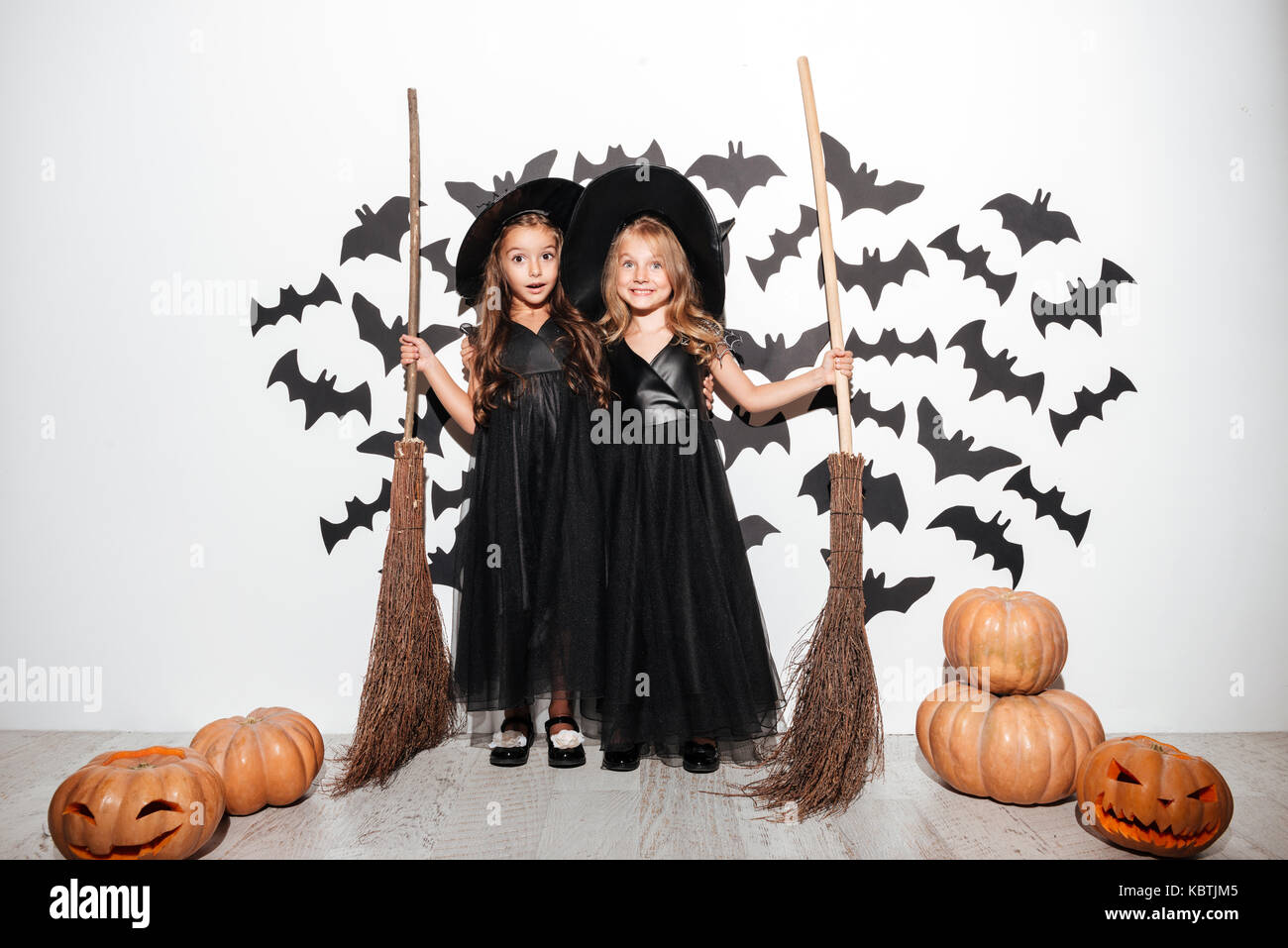 Couple de deux professionnels drôles de petites filles vêtues de costumes de Halloween tenue manches et posant avec les chauves-souris et les citrouilles sur un arrière-plan Banque D'Images