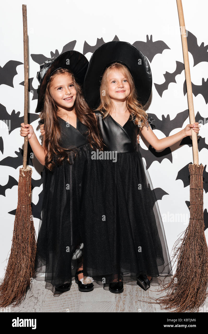 Couple de deux drôles de petites filles vêtues de costumes de Halloween tenue manches et posant avec les chauves-souris sur un arrière-plan Banque D'Images