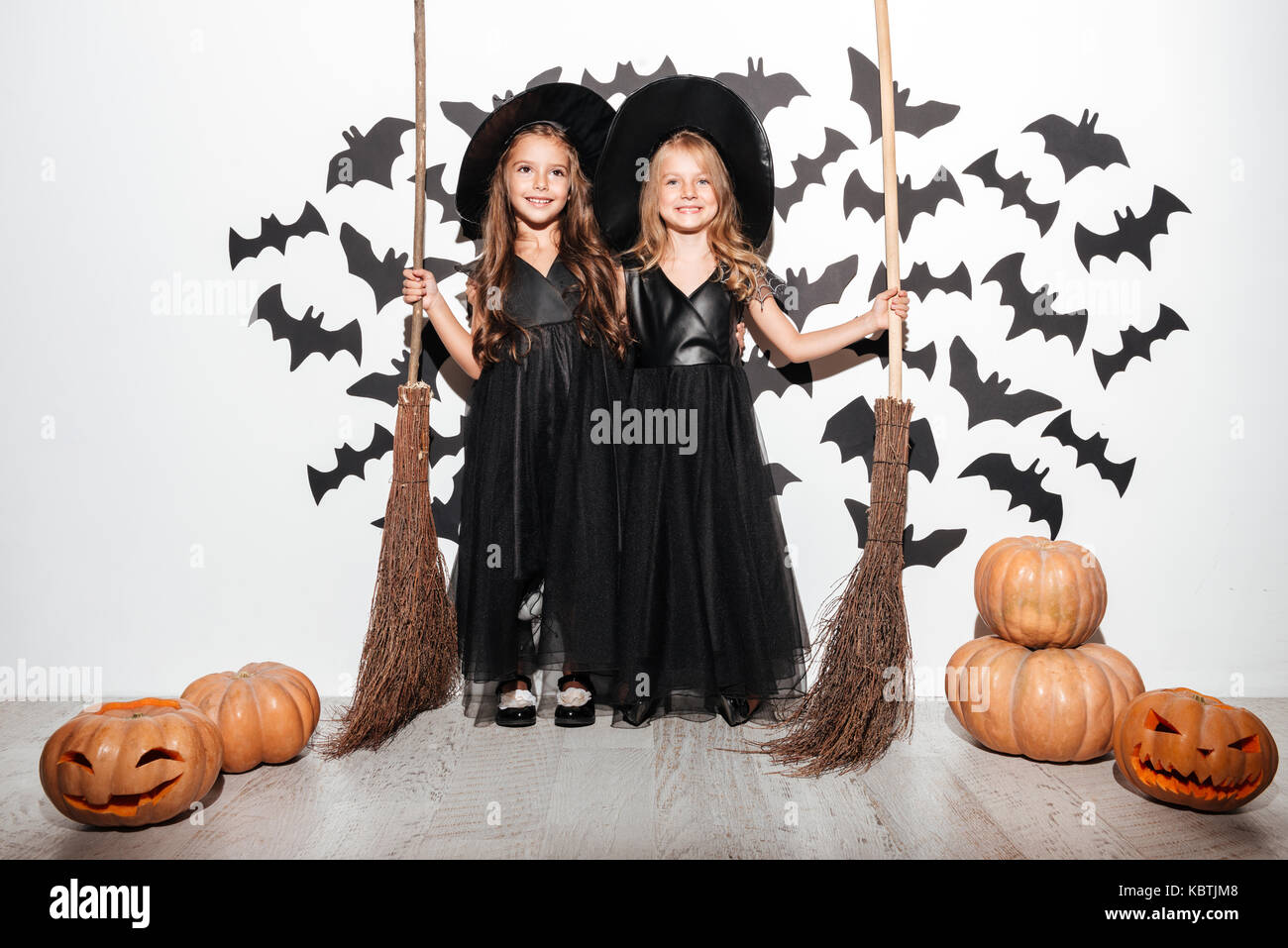 Couple de deux drôles de petites filles vêtues de costumes de Halloween tenue manches et posant avec les chauves-souris et les citrouilles sur un arrière-plan Banque D'Images