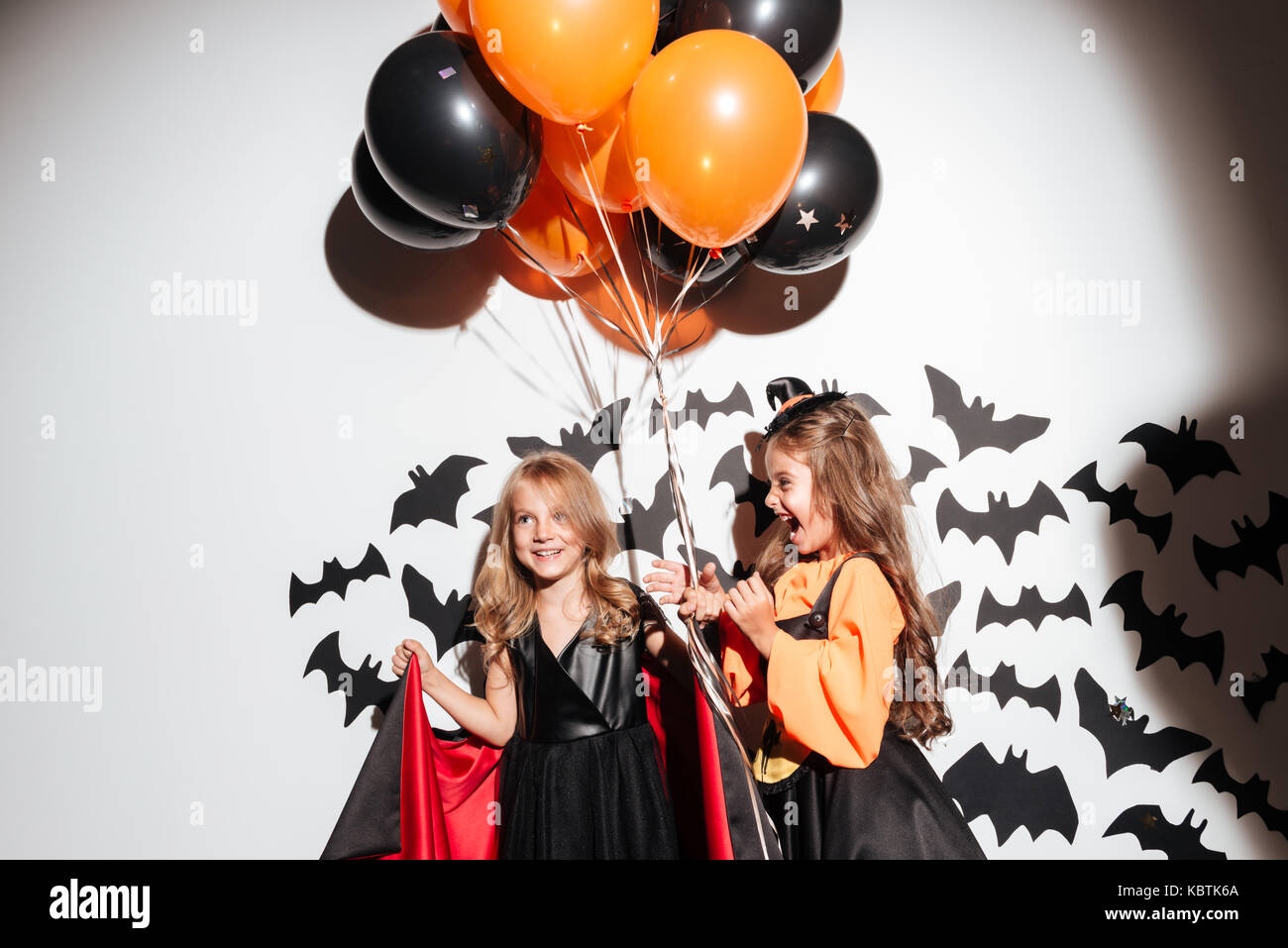 Couple de deux drôles de petites filles vêtues de costumes de halloween holding ballons dirigeables et posant avec les chauves-souris sur un arrière-plan Banque D'Images