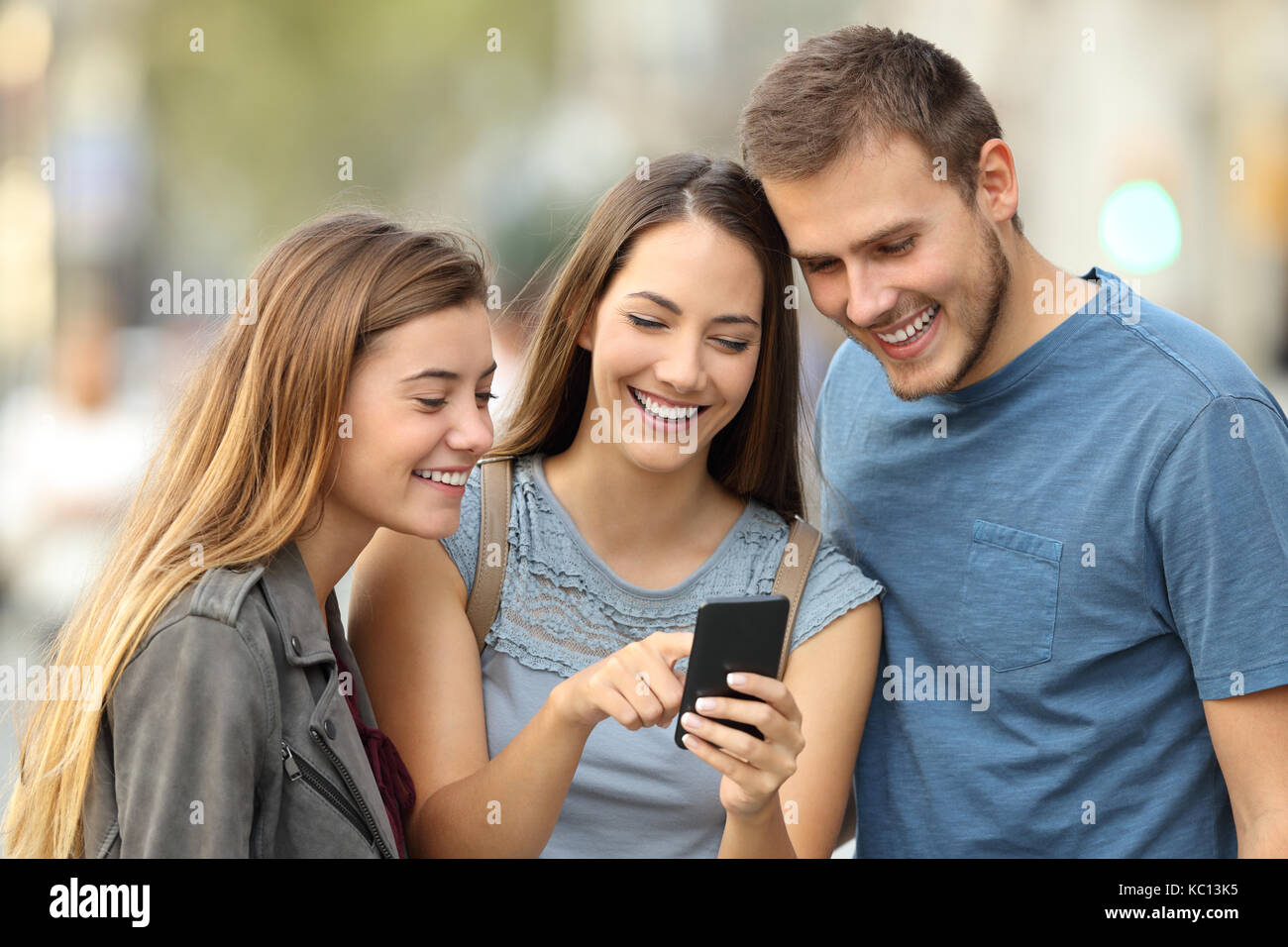 Heureux groupe de trois amis à l'aide d'un téléphone intelligent à l'extérieur permanent dans la rue Banque D'Images