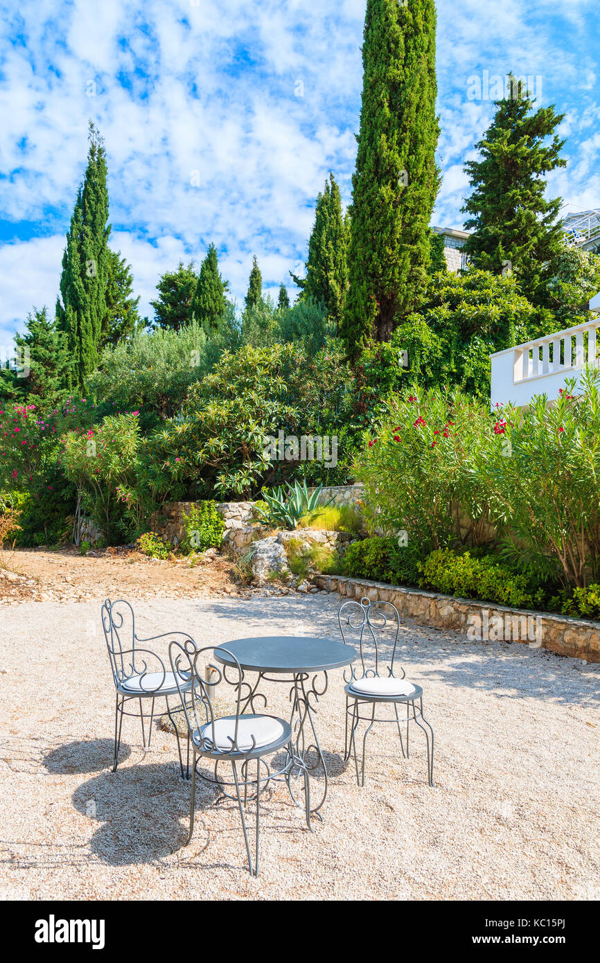Trois chaises en métal avec table sur le gravier dans le patio jardin méditerranéen, près de la ville de Primosten, Croatie, Dalmatie Banque D'Images