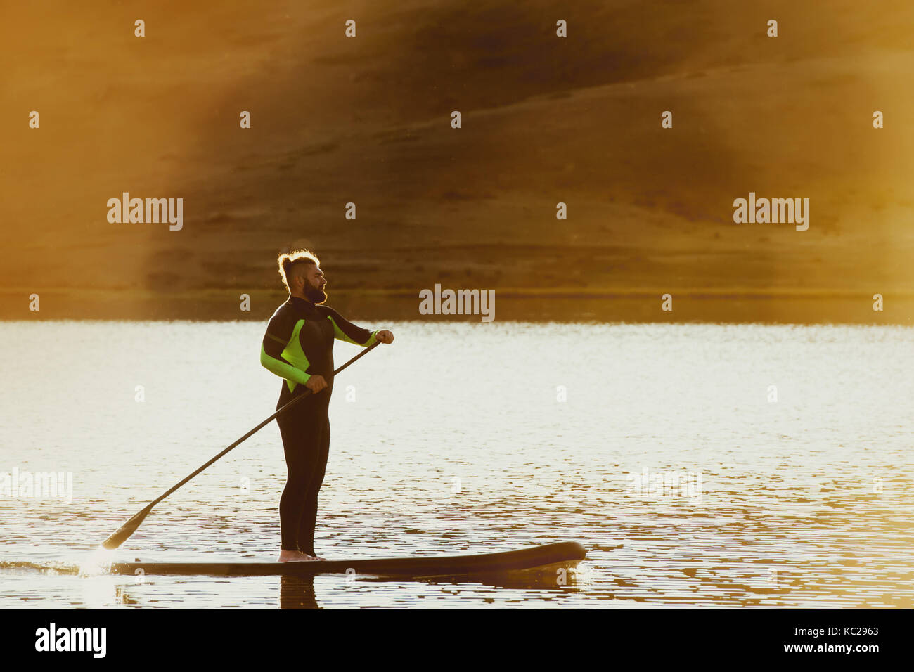 Homme nager sup paddle board coucher du soleil Banque D'Images